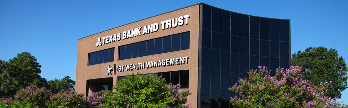 picture of building with blue sky around and green trees; words Texas Bank and Trust and TBT Wealth Management are on the building