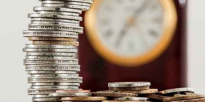 stack of coins in front of a clock