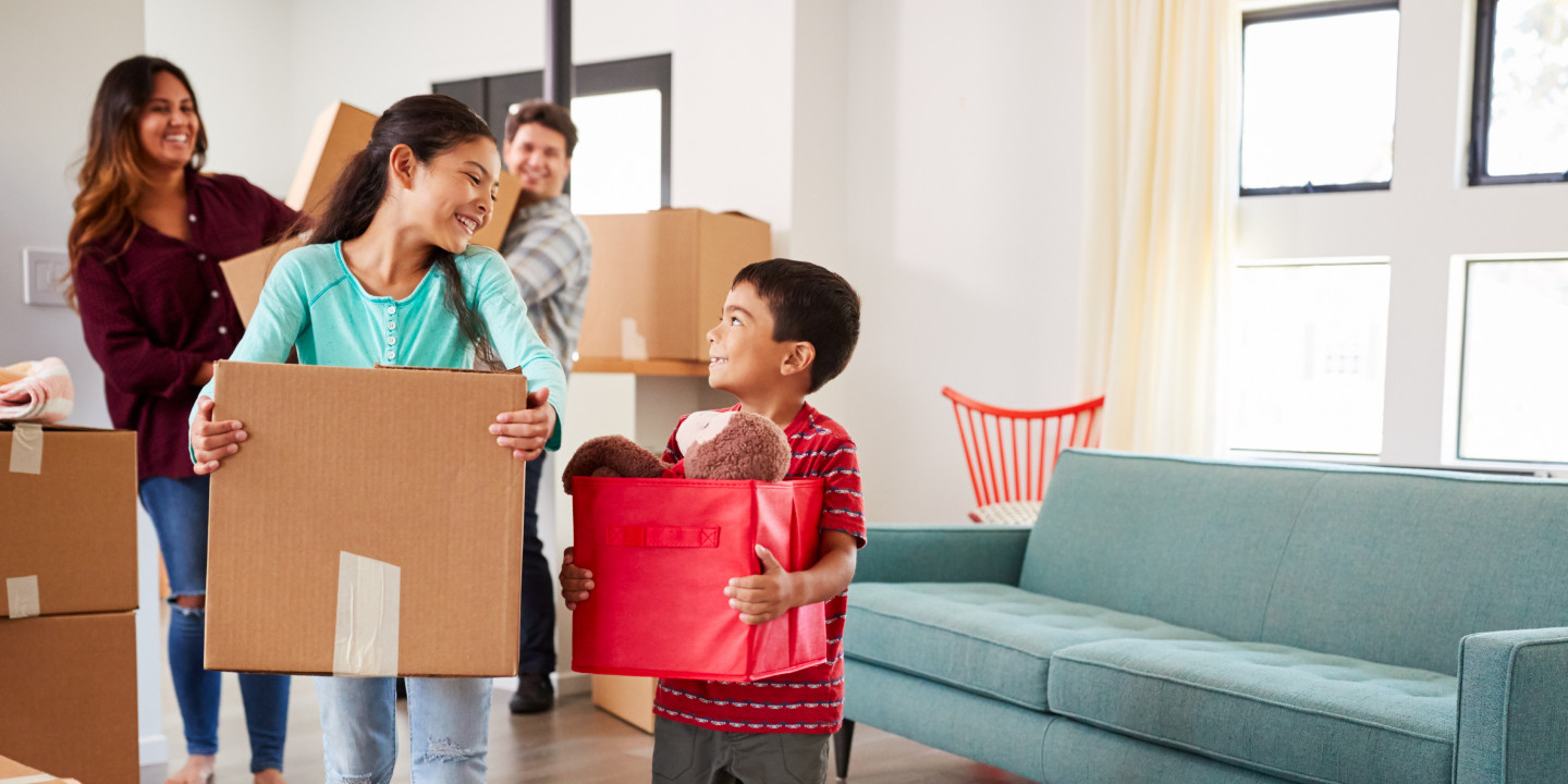 Family all smiling while moving into new home; all are carrying boxes