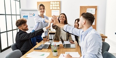 Group of young business people high-fiving while sitting around work table