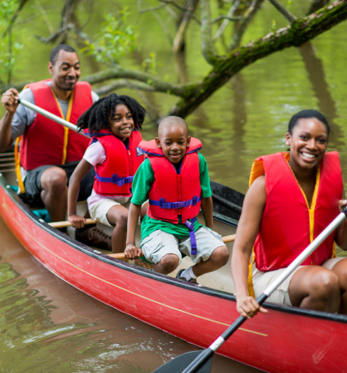 African American family of four smiling while canoeing; all wearing life jackets