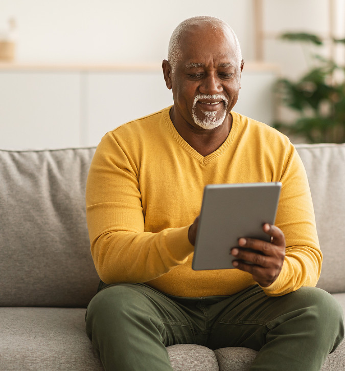 Older man, smiling, sitting on couch and using a tablet