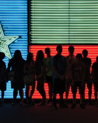 silhouettes of young people standing in front of large neon Texas flag